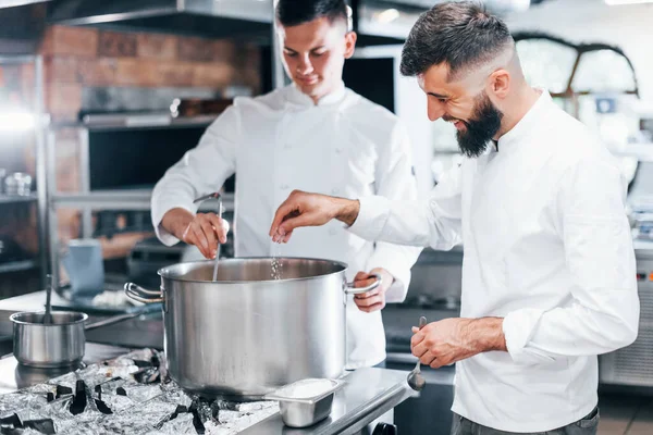 With help from other employee. Chef in white uniform cooking food at kitchen. Busy day at work.