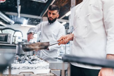 Beyaz üniformalı insanlar mutfakta birlikte yemek pişiriyorlar. İşte yoğun bir gün..