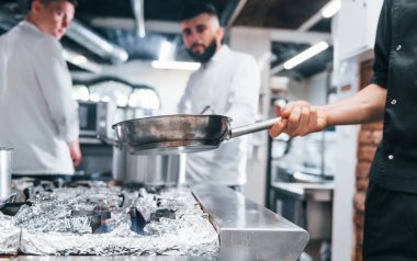Beyaz üniformalı insanlar mutfakta birlikte yemek pişiriyorlar. İşte yoğun bir gün..