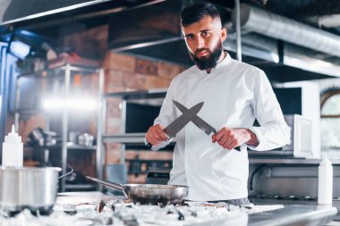 Mutfakta duran beyaz üniformalı şef. Ellerinde bıçak tutarak..