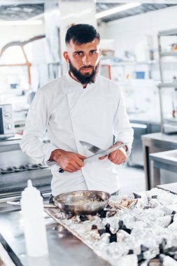 Mutfakta duran beyaz üniformalı şef. Ellerinde bıçak tutarak..