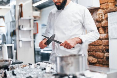 Mutfakta duran beyaz üniformalı şef. Ellerinde bıçak tutarak..
