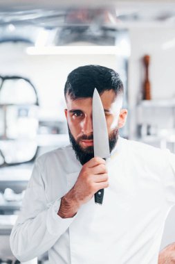 Mutfakta duran beyaz üniformalı şef. Ellerinde bıçak tutarak.