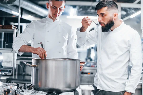 With help from other employee. Chef in white uniform cooking food at kitchen. Busy day at work.