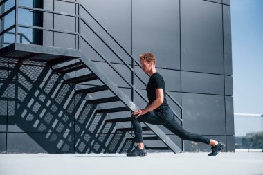 Siyah binanın yakınında ısınıyorum. Açık havada siyah gömlekli ve pantolonlu genç bir adam..