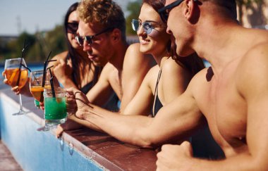 Konuşmak ve içmek. Bir grup mutlu genç gündüz yüzme havuzunda eğleniyor..