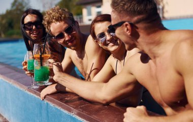 Konuşmak ve içmek. Bir grup mutlu genç gündüz yüzme havuzunda eğleniyor..
