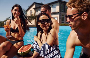 Güneşli sıcak hava. Bir grup mutlu genç gündüz yüzme havuzunda eğleniyor..