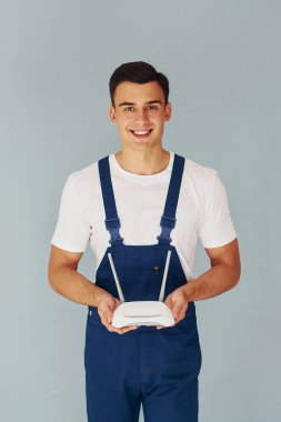 Wi-fi yönlendirici tutuyor. Mavi üniformalı erkek işçi beyaz arka planda stüdyonun içinde duruyor..