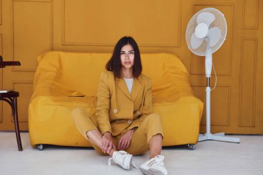 Kadın turuncu renkli odada oturuyor. Aynı renkli kıyafetlerle..