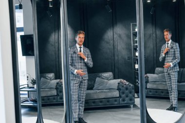 Aynaya bakıyor. Modern mağazada yeni kıyafetleri olan genç bir adam. Erkekler için pahalı bir elbise..