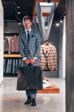 Modern mağazada yeni kıyafetleri olan genç bir adam. Erkekler için pahalı bir elbise..