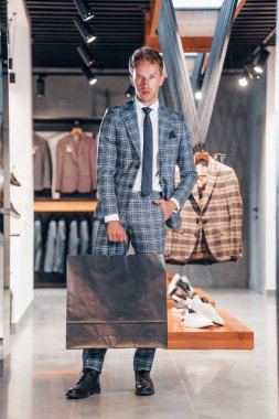 Çantayı satışta tutuyor. Modern mağazada yeni kıyafetleri olan genç bir adam. Erkekler için pahalı bir elbise..
