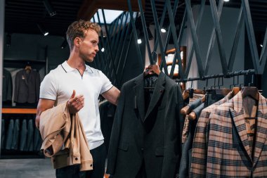 Ceket arıyor. Modern mağazada yeni kıyafetleri olan genç bir adam. Erkekler için pahalı bir elbise..