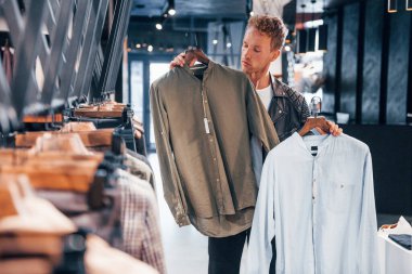 Büyük seçim. Modern mağazada yeni kıyafetleri olan genç bir adam. Erkekler için pahalı bir elbise..