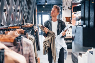 Büyük seçim. Modern mağazada yeni kıyafetleri olan genç bir adam. Erkekler için pahalı bir elbise..