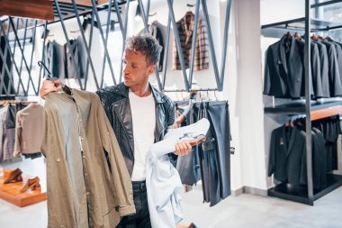 Büyük seçim. Modern mağazada yeni kıyafetleri olan genç bir adam. Erkekler için pahalı bir elbise..