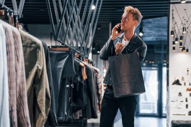 Telefonla konuşuyor. Modern mağazada yeni kıyafetleri olan genç bir adam. Erkekler için pahalı bir elbise..