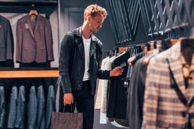 Güzel siyah ceketli. Modern mağazada yeni kıyafetleri olan genç bir adam. Erkekler için pahalı bir elbise..