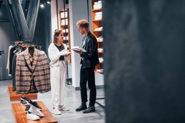 Genç bayan işçi, modern mağazada erkeklerin pahalı giysilerini seçmesine yardım ediyor..