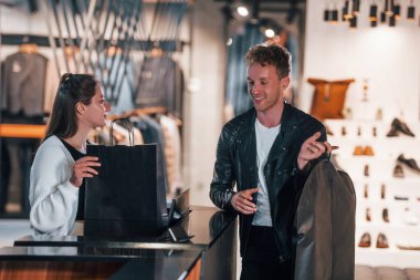 İnsanlar modern mağazadan zarif giysilerle alışveriş yapıyorlar. Kadın işçi kasadaki adama servis yapıyor..