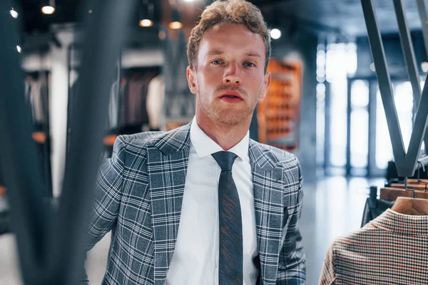 Giyinmeyi deniyor. Modern mağazada yeni kıyafetleri olan genç bir adam. Erkekler için pahalı bir elbise..