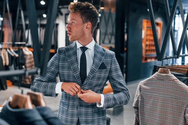 Giyinmeyi deniyor. Modern mağazada yeni kıyafetleri olan genç bir adam. Erkekler için pahalı bir elbise..