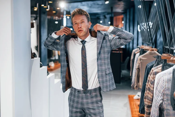 Giyinmeyi deniyor. Modern mağazada yeni kıyafetleri olan genç bir adam. Erkekler için pahalı bir elbise..