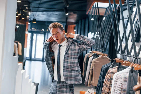 Giyinmeyi deniyor. Modern mağazada yeni kıyafetleri olan genç bir adam. Erkekler için pahalı bir elbise..