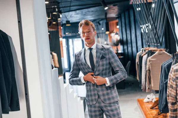Giyinmeyi deniyor. Modern mağazada yeni kıyafetleri olan genç bir adam. Erkekler için pahalı bir elbise..