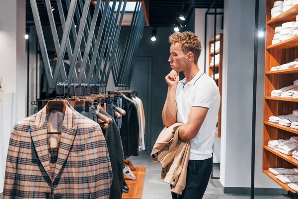 Giyinmeyi deniyor. Modern mağazada yeni kıyafetleri olan genç bir adam. Erkekler için pahalı bir elbise..