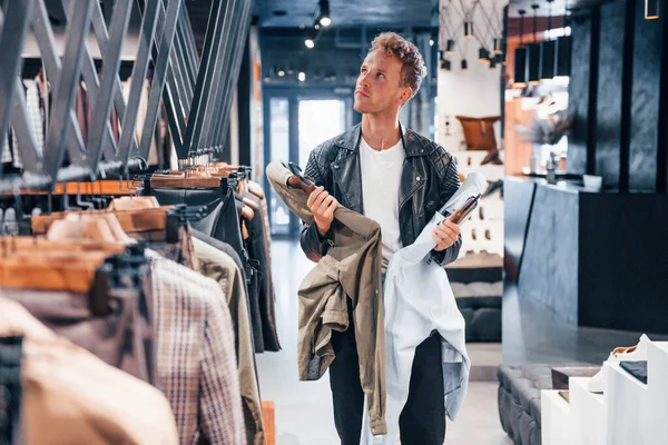 Büyük seçim. Modern mağazada yeni kıyafetleri olan genç bir adam. Erkekler için pahalı bir elbise..