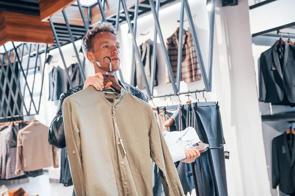 Büyük seçim. Modern mağazada yeni kıyafetleri olan genç bir adam. Erkekler için pahalı bir elbise..