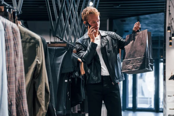Telefonla konuşuyor. Modern mağazada yeni kıyafetleri olan genç bir adam. Erkekler için pahalı bir elbise..