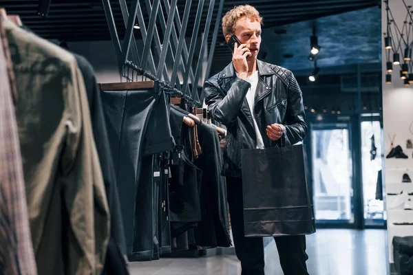Talks by the phone. Young guy in modern store with new clothes. Elegant expensive wear for men.