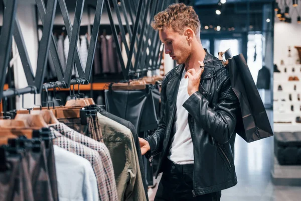 Büyük seçim. Modern mağazada yeni kıyafetleri olan genç bir adam. Erkekler için pahalı bir elbise..