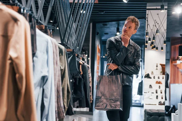 Büyük seçim. Modern mağazada yeni kıyafetleri olan genç bir adam. Erkekler için pahalı bir elbise..