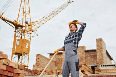 Ellerinde kürekle. Üniformalı inşaat işçisi ve güvenlik ekipmanı inşaatında çalışıyor.