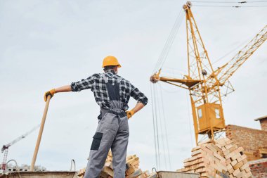 Ellerinde kürekle. Üniformalı inşaat işçisi ve güvenlik ekipmanı inşaatında çalışıyor.