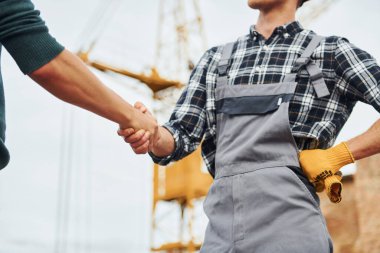 Tokalaşıyorum. Üniformalı ve güvenlik ekipmanlı iki inşaat işçisi birlikte iş yapıyorlar..