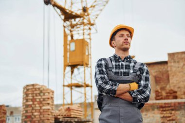 Kollarını kavuşturarak. Üniformalı inşaat işçisi ve güvenlik ekipmanı inşaatında çalışıyor.