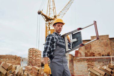 Merdiven ellerinde. Üniformalı inşaat işçisi ve güvenlik ekipmanı inşaatında çalışıyor.