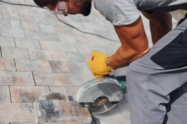 Dairesel testere kullanıyor. Sarı üniformalı erkek işçi kaldırımda çalışıyor..