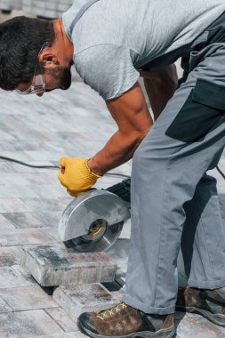 Dairesel testere kullanıyor. Sarı üniformalı erkek işçi kaldırımda çalışıyor..