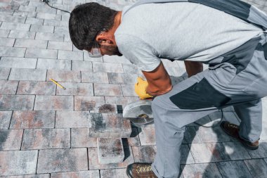 Dairesel testere kullanıyor. Sarı üniformalı erkek işçi kaldırımda çalışıyor..