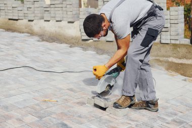 Dairesel testere kullanıyor. Sarı üniformalı erkek işçi kaldırımda çalışıyor..