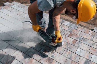 Dairesel testere kullanıyor. Sarı üniformalı erkek işçi kaldırımda çalışıyor..