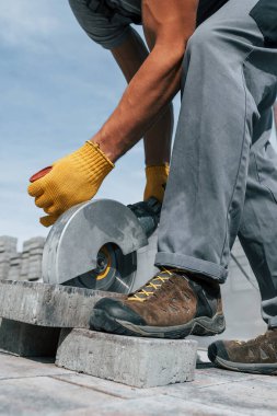 Dairesel testereyle dilimleniyor. Sarı üniformalı erkek işçi kaldırımda çalışıyor..