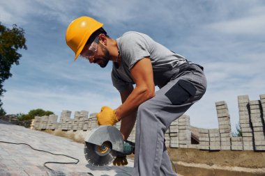Dairesel testereyle dilimleniyor. Sarı üniformalı erkek işçi kaldırımda çalışıyor..
