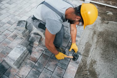 Lastik çekiç kullanıyor. Sarı üniformalı erkek işçi kaldırımda çalışıyor..